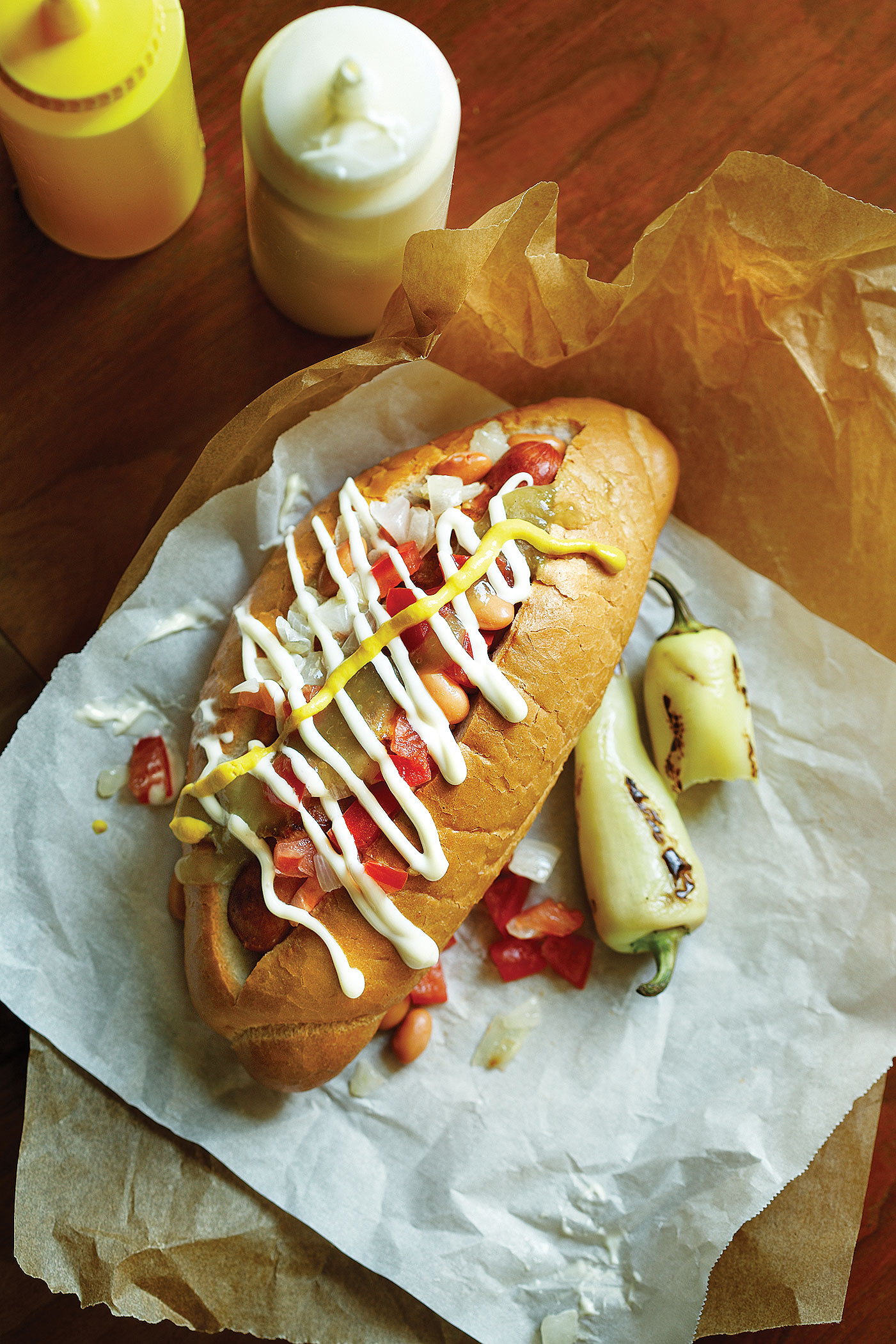 Gourmet dirty hot dog sandwich with various garnish on black slate