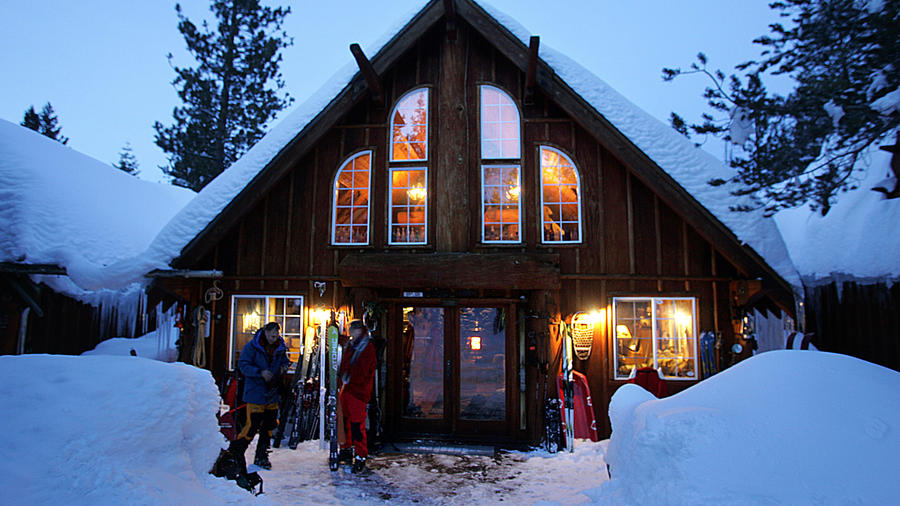 A cabin covered in snow at Lost Trail Lodge in Truckee with skiers standing outside
